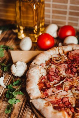 Arka planda sosisli pizza. Peynir, domates, baharat ve masada şeffaf bir şişe zeytinyağı.