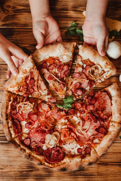 Çocuklar pizzayı salam ve mozzarella ile yerler. Tahta masa üzerinde İtalyan pizzası kesen ve yiyen insanlar.