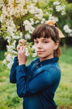 Kiraz çiçekleri. Tıbbi maskeli küçük kız ağaçtaki çiçeklere hayran. Dışarıda.