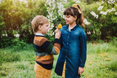 Pamuk elbise giymiş güzel bir kız ve ellerinde karahindiba tutan küçük bir çocuk. Arkadaşlık kavramı. Gün batımı