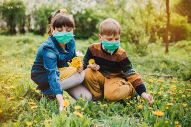 Erkek ve kız tıbbi maske takıyor, arka planda çiçekler. Koruyucu maskeli çocuklar. COVID-19 'a karşı tehlike ve güvenlik karantinası tedbirleri uyarısı.