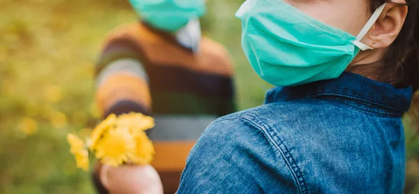Erkek ve kız tıbbi maske takıyor, arka planda çiçekler. Koruyucu maskeli çocuklar. COVID-19 'a karşı tehlike ve güvenlik önlemleri uyarısı. Koronavirüs salgını.