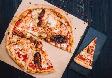 Taze kurutulmuş domatesli ev yapımı pizza, siyah taşlı arka planda tavuk, peynir ve biber.