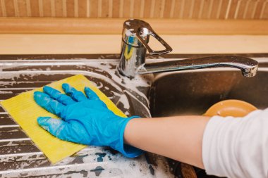 Mavi lastik eldivenli bir kadın mutfakta lavaboyu fırçalar. Mutfakta lavaboyu yıkayan bir kadının ayrıntıları. Lavabonun üzerinde ev işi yapan kadın eller.