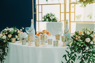 Gelin ve damadın düğün masası çiçeklerle ve mumlarla süslenmiş. Kapalı alanda düğün töreni. Bir düğün dekorunun yakın çekim detayları