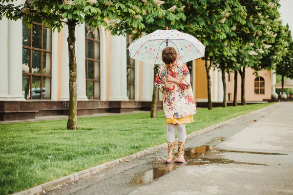 A beautiful girl in a bright rain jacket walks under an umbrella during the rain on the street. Soft focus. Happy childhood concept