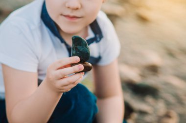 Kayaları tutan eller. Taşı açık havada elinde tutan küçük çocuğun yakın çekimi. Taş plajı