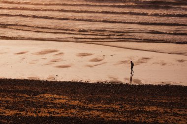 Gün batımında suyun yanında bir çocuğun silueti. Gün batımında sahilde oynayan bir çocuk.