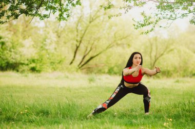 Güneşli bir günde çimlerin üzerinde açık havada yoga yapan genç bir kadın. Açık hava sporları. Tonus için egzersiz, esneklik