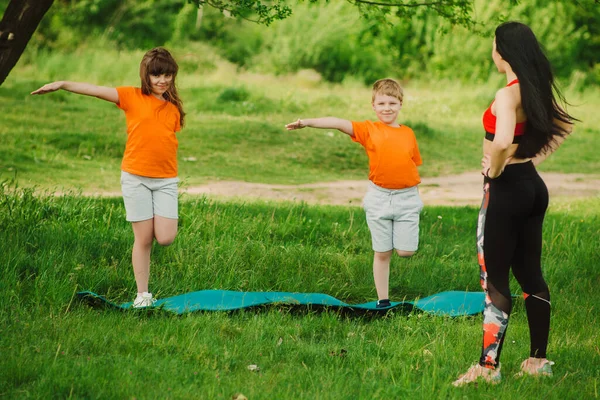 The coach helps children complete the exercise. Make sports open air. Healthy lifestyle concept. Baby yoga, fitness training.