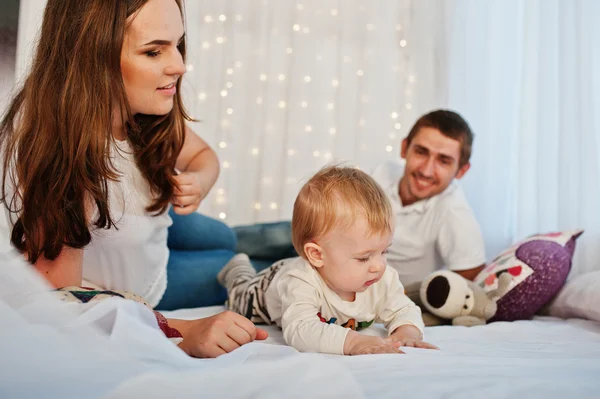 Mãe e pai com bebê menino deitado na cama branca com guirlanda — Fotografia de Stock