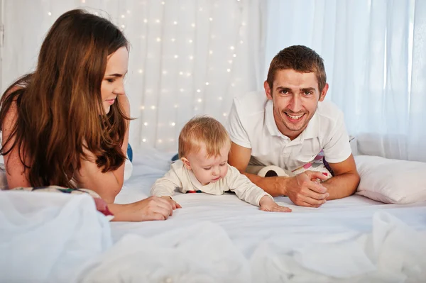 Mãe e pai com bebê menino deitado na cama branca com guirlanda — Fotografia de Stock