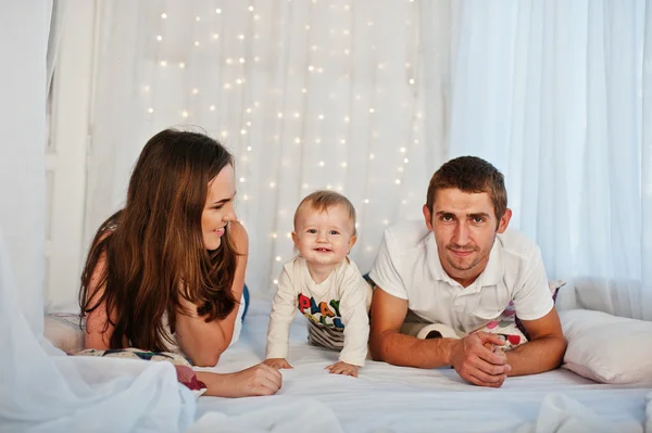 Mutter und Vater mit Baby auf weißem Bett mit Girlande liegend — Stockfoto