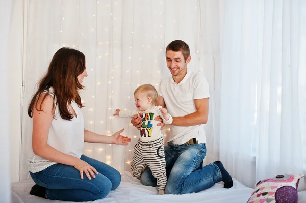 Mother and father with baby boy sitting on white bed with garlan — Stock Photo, Image