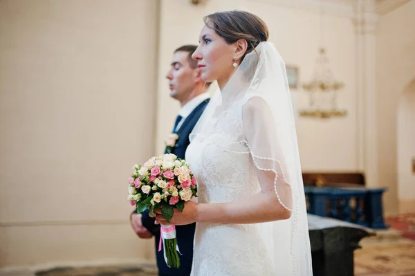 Wedding couple stay at church ceremony. Bride with bouquet at ha — Stock Photo, Image