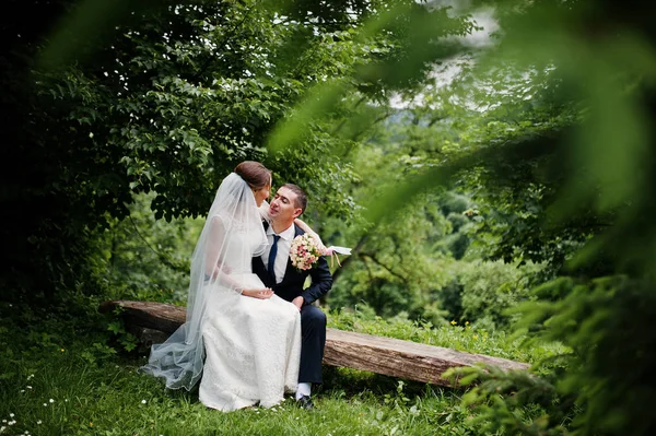 Hochzeitspaar sitzt auf Holzbank im Grünen — Stockfoto