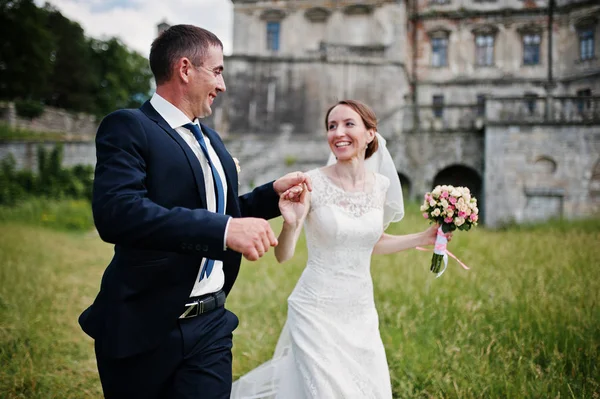 Hochzeitspaar läuft Händchen haltend hinter Schloss. — Stockfoto