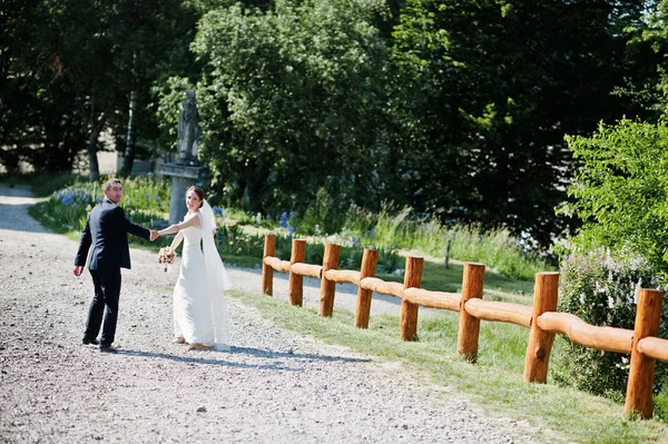Свадебная пара, идущая и держащаяся за руки на дороге — стоковое фото