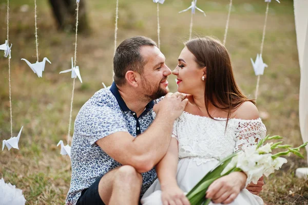 Feliz pareja embarazada sentada bajo la decoración arco en el jardín —  Fotos de Stock