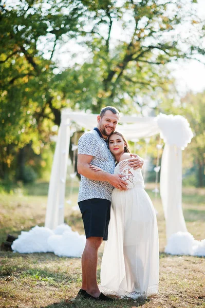 Feliz embarazada pareja estancia abrazo y amoroso cerca de arco de decoración en —  Fotos de Stock