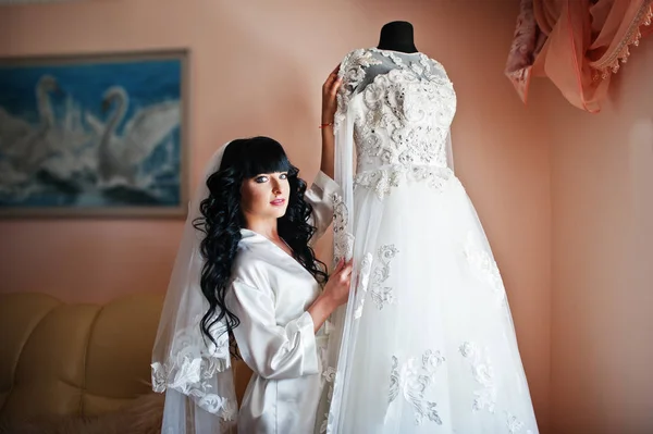 Giovane sposa bruna carino guardando il suo abito da sposa su manneq — Foto Stock