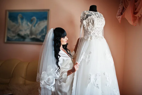 Молодая милая брюнетка невеста смотрит на свое свадебное платье на маннеке — стоковое фото