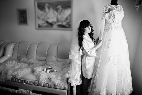 Junge süße brünette Braut betrachtet ihr Hochzeitskleid auf Schaufensterpuppe — Stockfoto