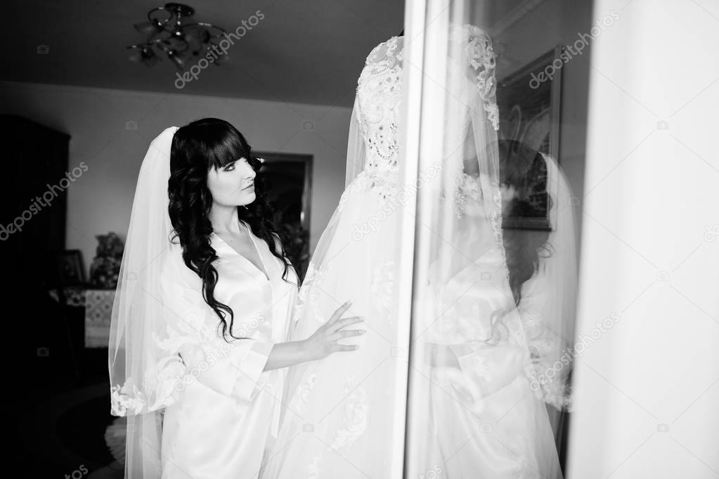 Young cute brunette bride looking at her wedding dress on manneq