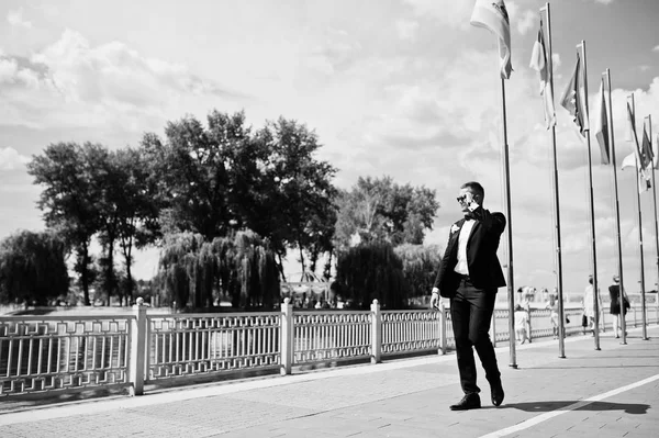 Elegante novio en gafas de sol caminando frente al mar de lago con bandera — Foto de Stock