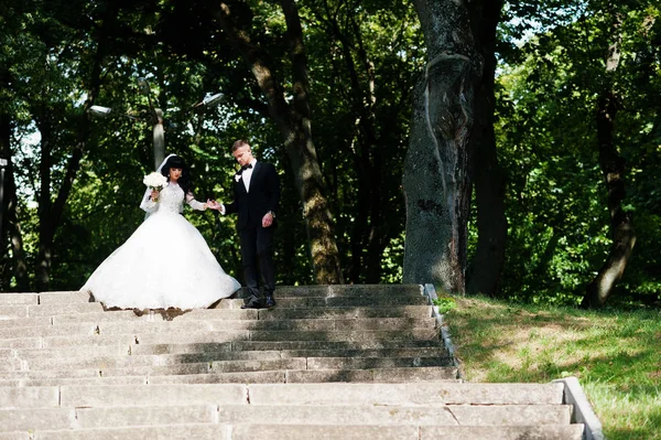 Nifty wedding couple at stairs on park at sunny wedding day. — Stock Photo, Image