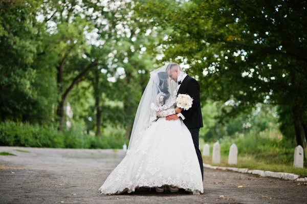 Sympatisk bröllop par bo och kyssar under slöja på park. — Stockfoto