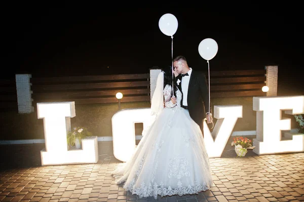 Élégant couple de mariage avec des ballons lumineux rester et baisers près — Photo