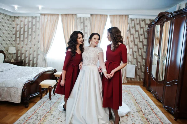 Noiva com duas damas de honra incríveis no vestido vermelho posado no quarto no — Fotografia de Stock