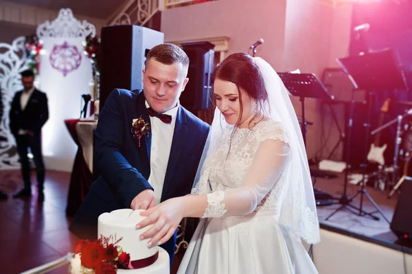 Γαμήλιο ζευγάρι κομμένα γαμήλια τούρτα με κόκκινα τριαντάφυλλα και κορδέλα — Φωτογραφία Αρχείου