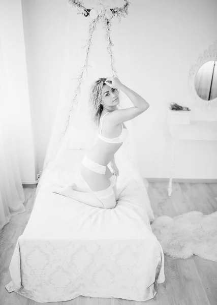 Curly menina loira em roupa interior sentado na cama quarto branco interior . — Fotografia de Stock