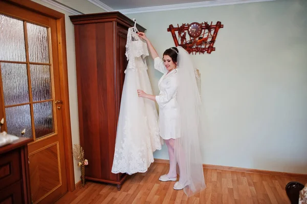 H を保持している絹のドレスの白いローブを着て笑顔のブルネットの花嫁 — ストック写真