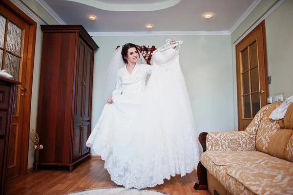 Lächelnde brünette Braut trägt auf weißem Seidenkleid Robe hält h — Stockfoto