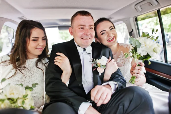 Feliz novio sonriente sentado en el coche de la boda con damas de honor . — Foto de Stock