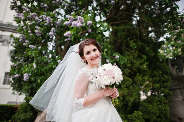 Linda novia morena bajo el árbol lila con ramo de boda en han —  Fotos de Stock