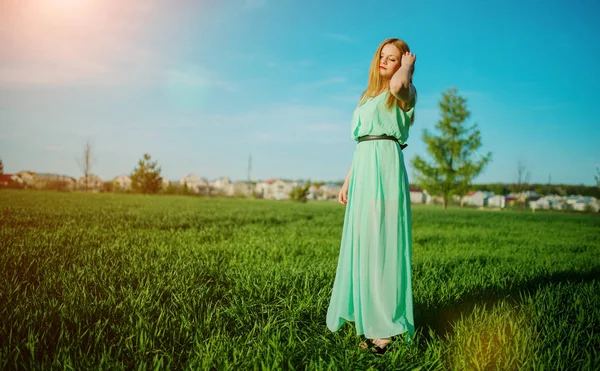 Kvinna i en vacker lång turkos klänning poserar på en äng på g — Stockfoto