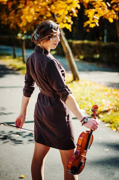 Портрет умной девушки со скрипкой на руках на открытом воздухе в коричневой коа — стоковое фото
