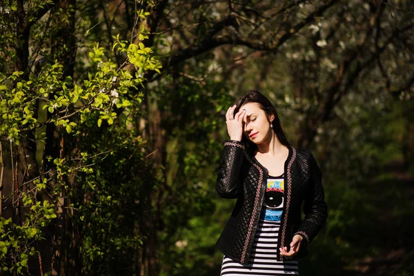 Chica morena en la chaqueta de cuero posado en el jardín de primavera. Caminando —  Fotos de Stock