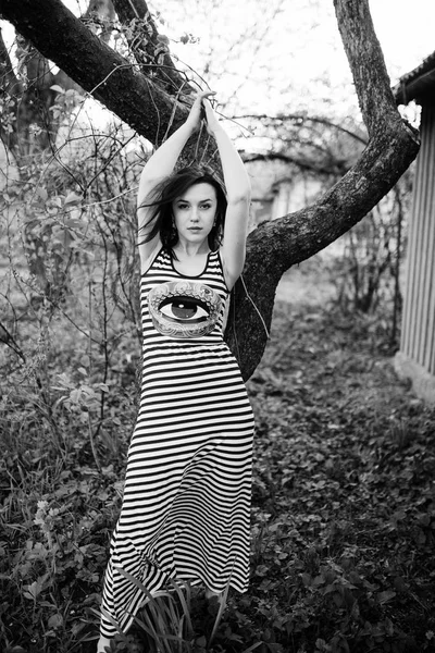 Brunette model meisje op jurk met strepen stelde in de buurt van boom. Zwart — Stockfoto