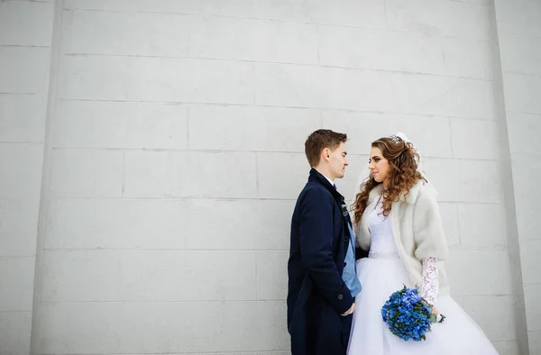 Unga bröllopsparet på kall vinterdag mot vit sten vägg — Stockfoto