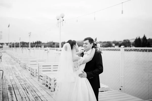 Das Hochzeitspaar bleibt bei bewölktem Himmel auf dem Steg. schwarz-weiß — Stockfoto