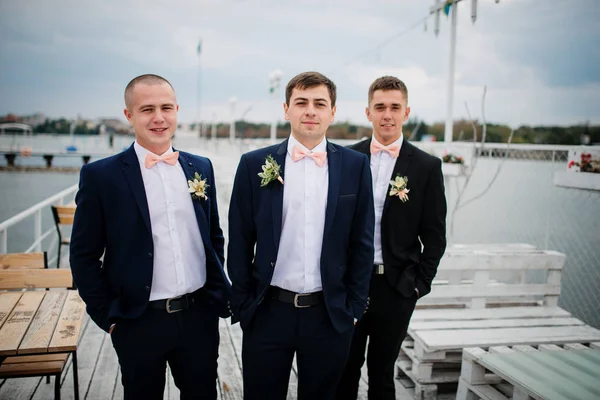 Groom avec les meilleurs hommes posés sur la jetée d'amarrage à nuageux mariage d — Photo