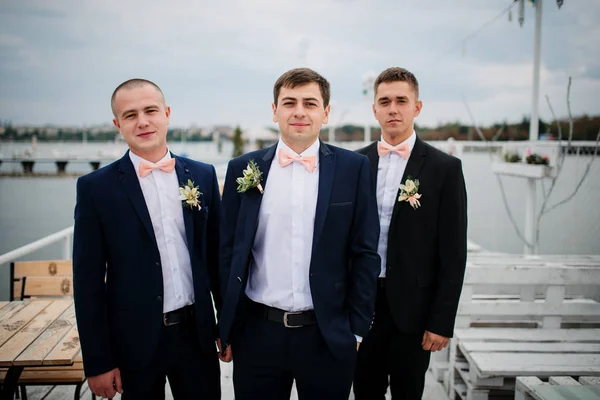 Groom avec les meilleurs hommes posés sur la jetée d'amarrage à nuageux mariage d — Photo