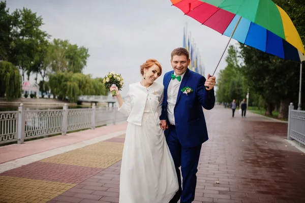 Verliebtes Hochzeitspaar unter buntem Regenschirm bei Regen. — Stockfoto