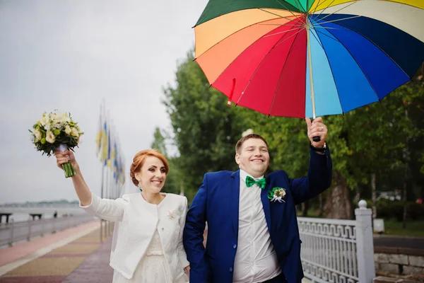 Verliebtes Hochzeitspaar unter buntem Regenschirm bei Regen. — Stockfoto