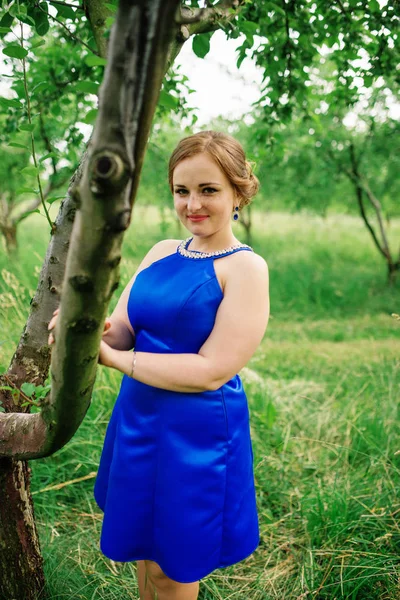 Νέοι υπέρβαρα κορίτσι το μπλε φόρεμα που θέτει φόντο άνοιξη gard — Φωτογραφία Αρχείου